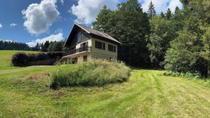 Una casa con balcón, rodeada de un campo cubierto de hierba y árboles.