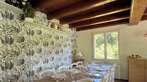 Un comedor con una larga mesa de madera dispuesta para seis personas, sillas blancas y papel tapiz estampado.