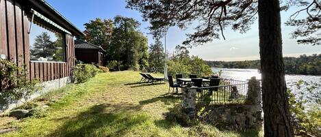 Un espace extérieur verdoyant, avec un mur de pierre, un bâtiment en bois et une vue sur un lac.