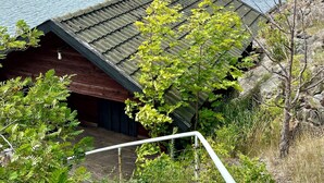 A cabin with a metal roof, surrounded by greenery and overlooking a lake.