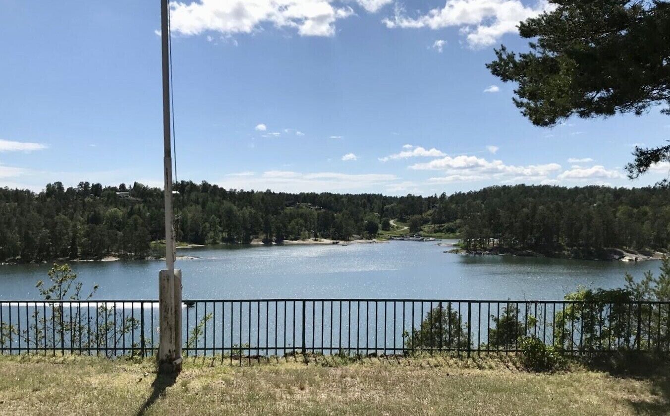 A lakeside view with a metal fence, trees, and a clear sky.