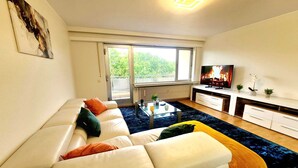 A modern living room with a sofa, a coffee table, a TV, and a balcony view. - New 2bedrooms in Center Terrace&Parking (Luxembourg City)