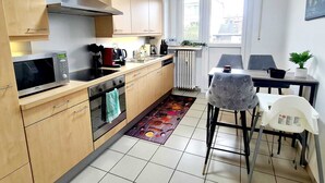 A compact kitchen with wooden cabinets, a microwave, a stove, and a small dining area with a table and chairs. - New 2bedrooms in Center Terrace&Parking (Luxembourg City)
