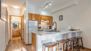 Une cuisine moderne avec des meubles en bois, un grand îlot central doté de tabourets, un réfrigérateur et un four à micro-ondes.