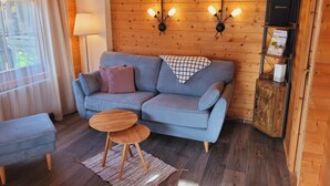 Et hyggeligt rum med en grå sofa, et lille rundt træbord og en lampe.