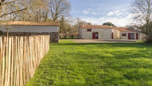 A rural property with a stone wall, a fenced yard, and two buildings with red shutters.