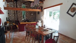 A rustic dining area with a wooden table and chairs, a stone wall, and a large window allowing natural light.