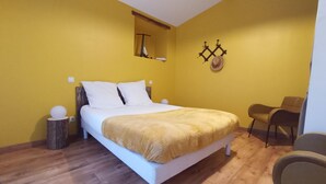 A bedroom with a bed, a chair, a wooden floor, and a yellow wall.