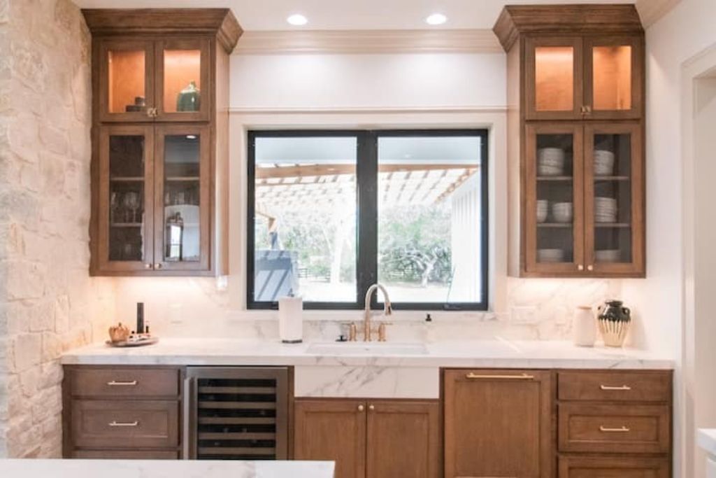 A kitchen with wooden cabinets, a marble countertop, and a window with a view of greenery.
