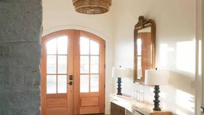 A hallway with a stone archway, wooden door, and a mirror above a wooden console table with two lamps. - RMB Longhorn West, luxury living in the country (Weimar)