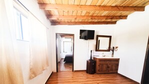 Een kamer met houten vloer, houten plafond, een bed, een televisie, een spiegel en een houten kast.