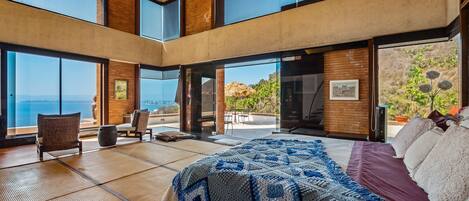 A spacious bedroom with a large bed, a view of the ocean, and a balcony with outdoor seating.