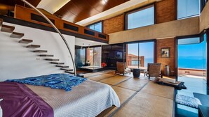 A modern hotel room with a large bed, a view of the sea, a balcony with seating, and a staircase. - Exclusive Master Suite - Casa Samo (Puerto Vallarta)