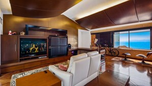 A modern living room with a large flat-screen TV, comfortable seating, a bike, and a view of the ocean. - Exclusive Master Suite - Casa Samo (Puerto Vallarta)