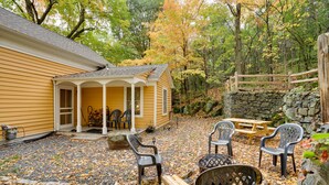 A yellow house with a porch, outdoor seating, and a stone wall.