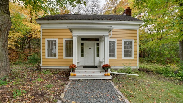 A two-story house with a front porch, a gravel driveway, and a garden with pumpkins.
