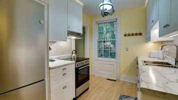 A kitchen with white cabinets, a stove, an oven, a sink, and a window with a view of trees.