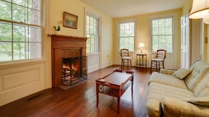 A room with a fireplace, wooden flooring, a sofa, and two chairs.