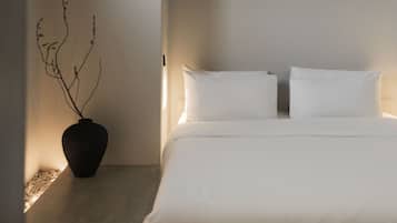 Une chambre à coucher au style minimaliste, avec un lit, des oreillers blancs et un vase décoré de branches.