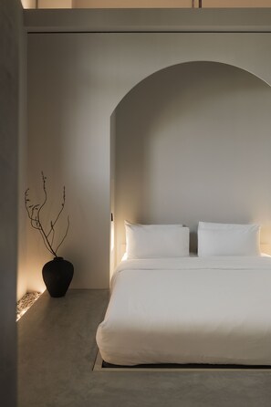 A minimalist bedroom with a bed, white pillows, and a vase with branches. - Kodō Hotel (Los Angeles)