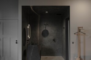 A modern bathroom with a minimalist design, featuring a large mirror, a round light fixture, and a wooden hanger on the wall. - Kodō Hotel (Los Angeles)