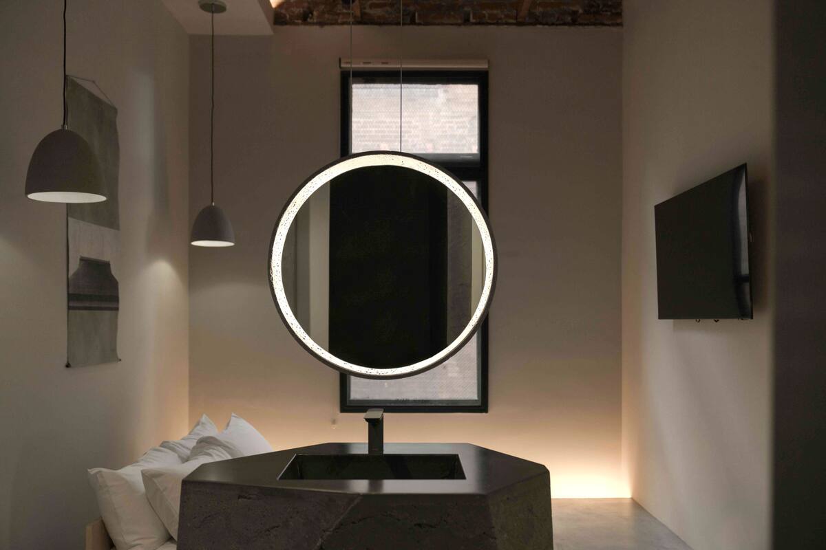 A modern bathroom with a round mirror, pendant lights, and a large window.