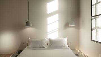 A minimalist bedroom with a large bed, two pendant lights, and a view of the outside through a window.