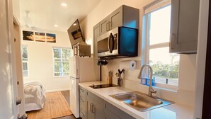 A modern kitchen with grey cabinets, a stainless steel sink, and a built-in microwave. - Brand New Studio with Sunset View (Haleiwa)