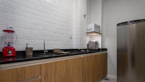 A modern kitchen with white subway tiles, a stainless steel refrigerator, a red blender, and wooden cabinets.