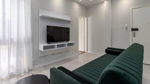 A modern living room with a flat-screen TV mounted on a white wall, a green sofa, and a small table.