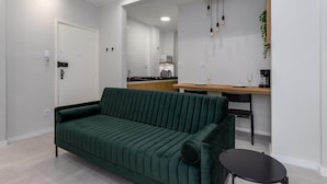 A modern living room with a green sofa, a small black table, and a kitchen area in the background.