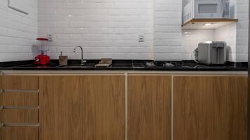 A modern kitchen with white subway tiles, a black countertop, wooden cabinets, a red blender, a microwave, and a coffee maker.