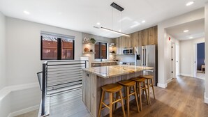 Eine moderne Küche mit einer zentralen Kochinsel, Barhocker und Blick in den Garten durch ein Fenster.