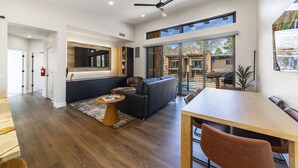 A spacious living area with a large window, a ceiling fan, and a dining area with a wooden table and chairs.