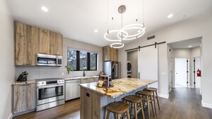 A modern kitchen with wooden cabinets, stainless steel appliances, and a marble island with bar stools.