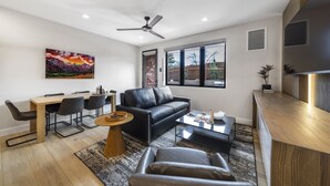 A modern living room with a black leather sofa, a dining table with chairs, a coffee table, and a ceiling fan.