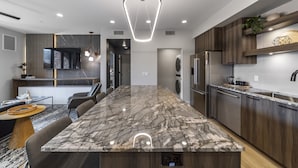 A modern kitchen with a marble island, built-in appliances, and a pendant light.