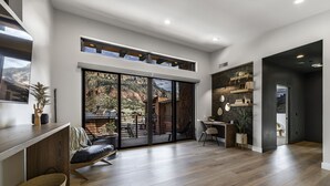 A spacious room with a large sliding glass door leading to a patio, a wooden floor, a desk with a chair, and a bookshelf. - LaFave-Luxury Villa at Zion: Johnson Mountain (Springdale)