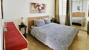 A bedroom with a bed, a ceiling fan, a painting, a nightstand, a lamp, and a window with curtains. - Relax in this comfortable apartment with Oceanview on the 21st floor (Luquillo)