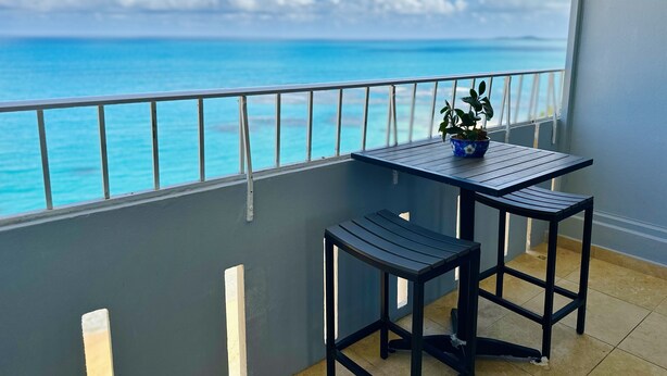 A balcony with a table and two chairs, overlooking a turquoise sea and a clear sky. - Relax in this comfortable apartment with Oceanview on the 21st floor (Luquillo)