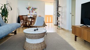A modern living room with a sofa, a wicker coffee table, a TV stand, and a dining area in the background. - Relax in this comfortable apartment with Oceanview on the 21st floor (Luquillo)