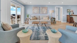Un salon spacieux avec un canapé bleu clair, un fauteuil assorti et une table basse dont le socle est fait de fibres tressées. Une grande fenêtre offre une vue sur l’extérieur.