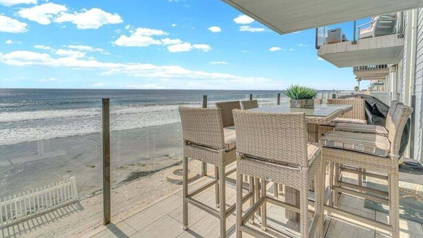 Un balcon meublé avec des meubles en osier, donnant sur une plage.
