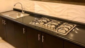 A modern kitchen with dark cabinetry, a stainless steel sink, and a gas stove. - ROOMIES HOSTEL - Calle Puebla (Mexico City)