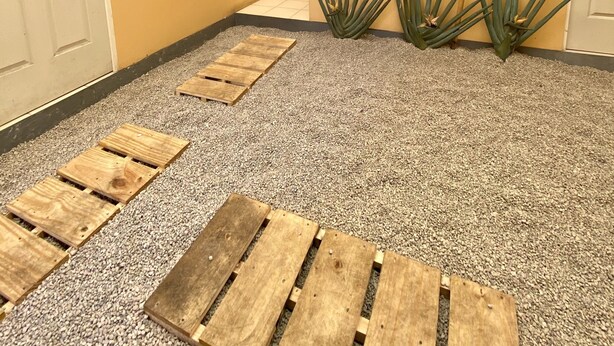 A hallway with a beige wall, a poster, and a small garden area with wooden pallets and agave plants. - ROOMIES HOSTEL - Calle Puebla (Mexico City)