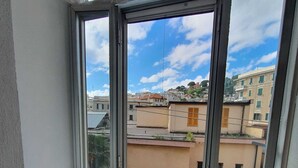 Un balcó amb una cadira de fusta, vista d'edificis i un cel serè.