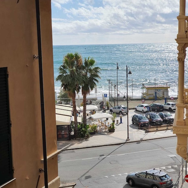 A coastal street with parked cars, a pedestrian area, and a view of the sea.