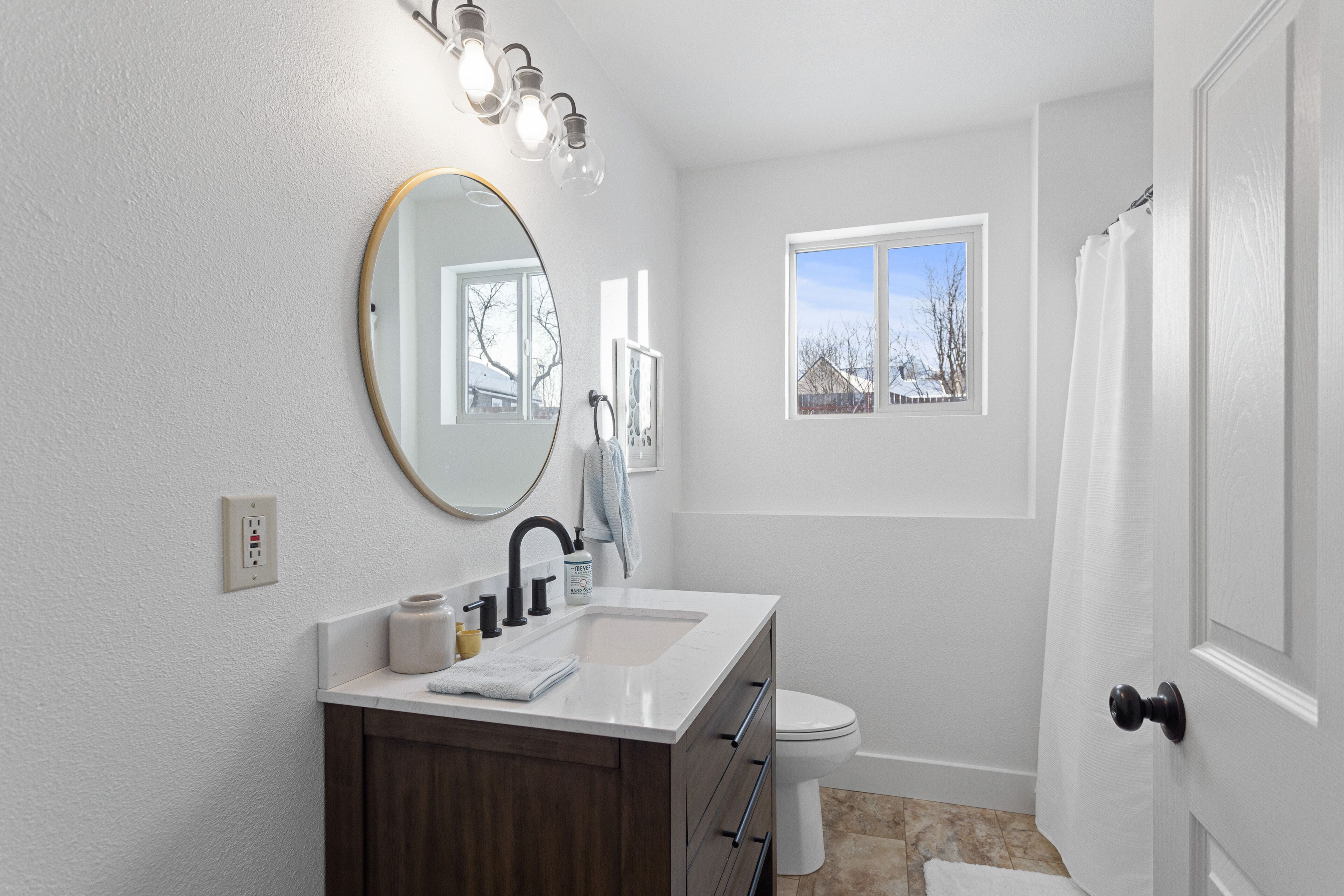 A bathroom with a white vanity, a round mirror, a sink, and a toilet.