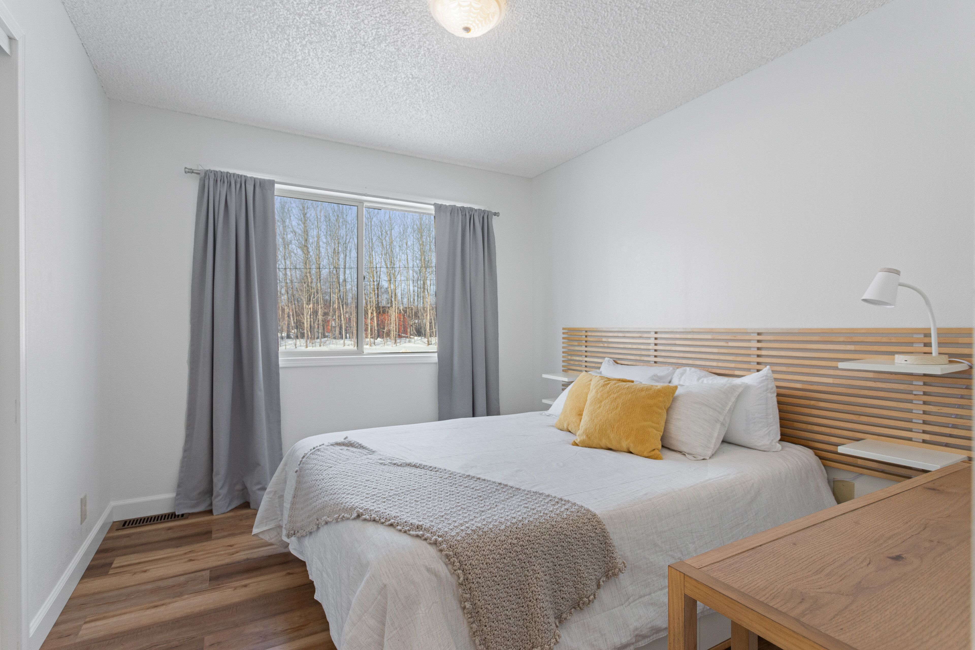 Un dormitorio con cama, mesita de noche, lámpara y ventana con cortinas.
