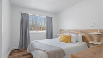 Un dormitorio con cama, mesita de noche, lámpara y ventana con cortinas.